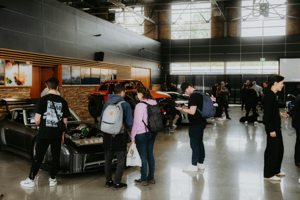 Visitors explore an indoor car exhibition featuring vintage and modified cars in a spacious hall.